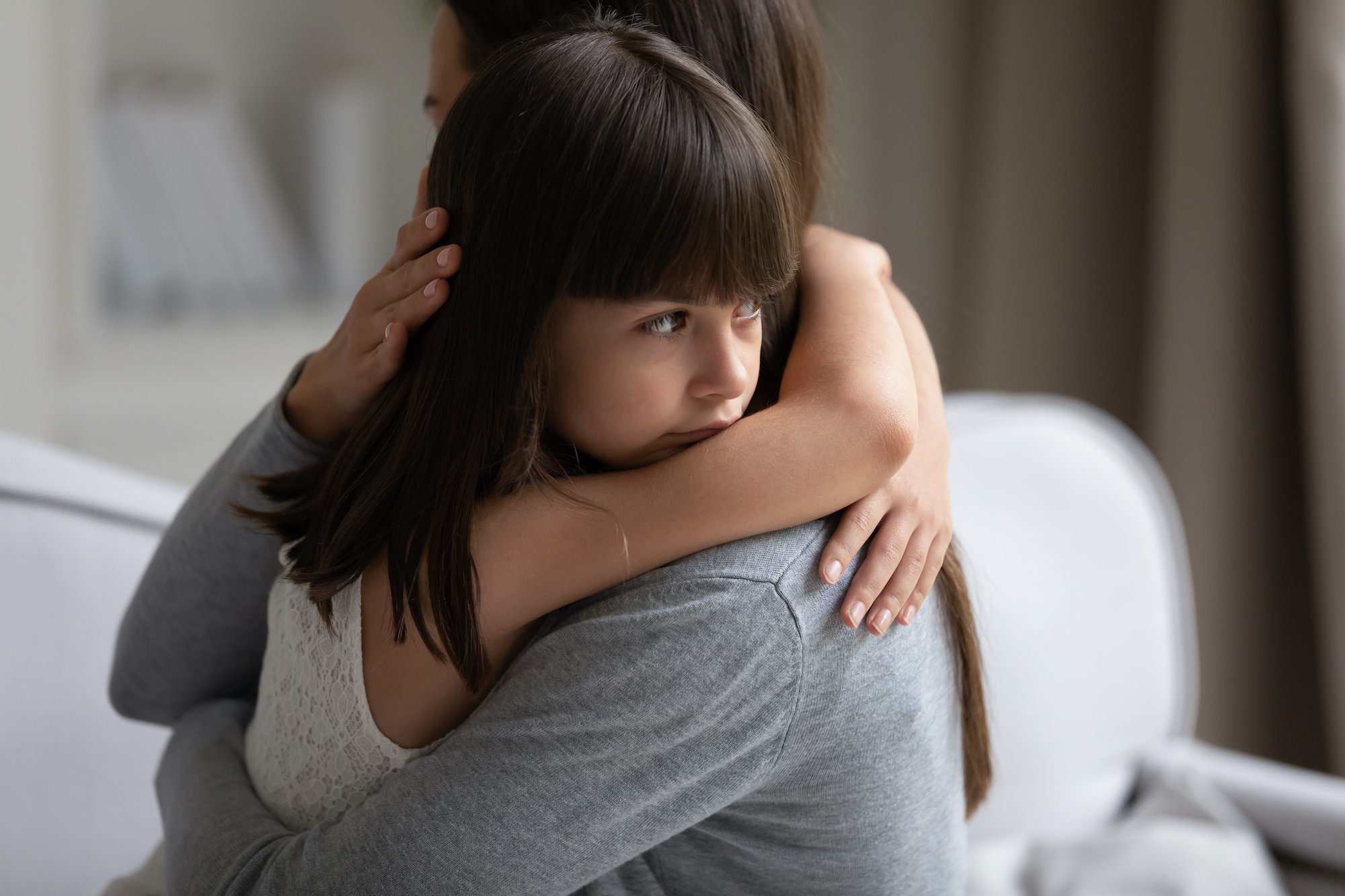 A little girl hugging a woman and lookin gsadly out over her shoulder