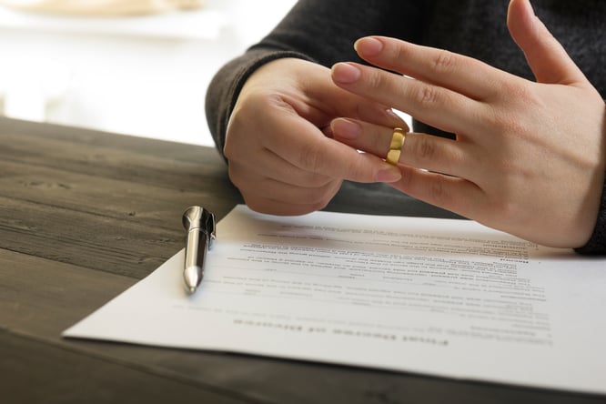 A person pulling off their wedding band with some documents spread out on the table