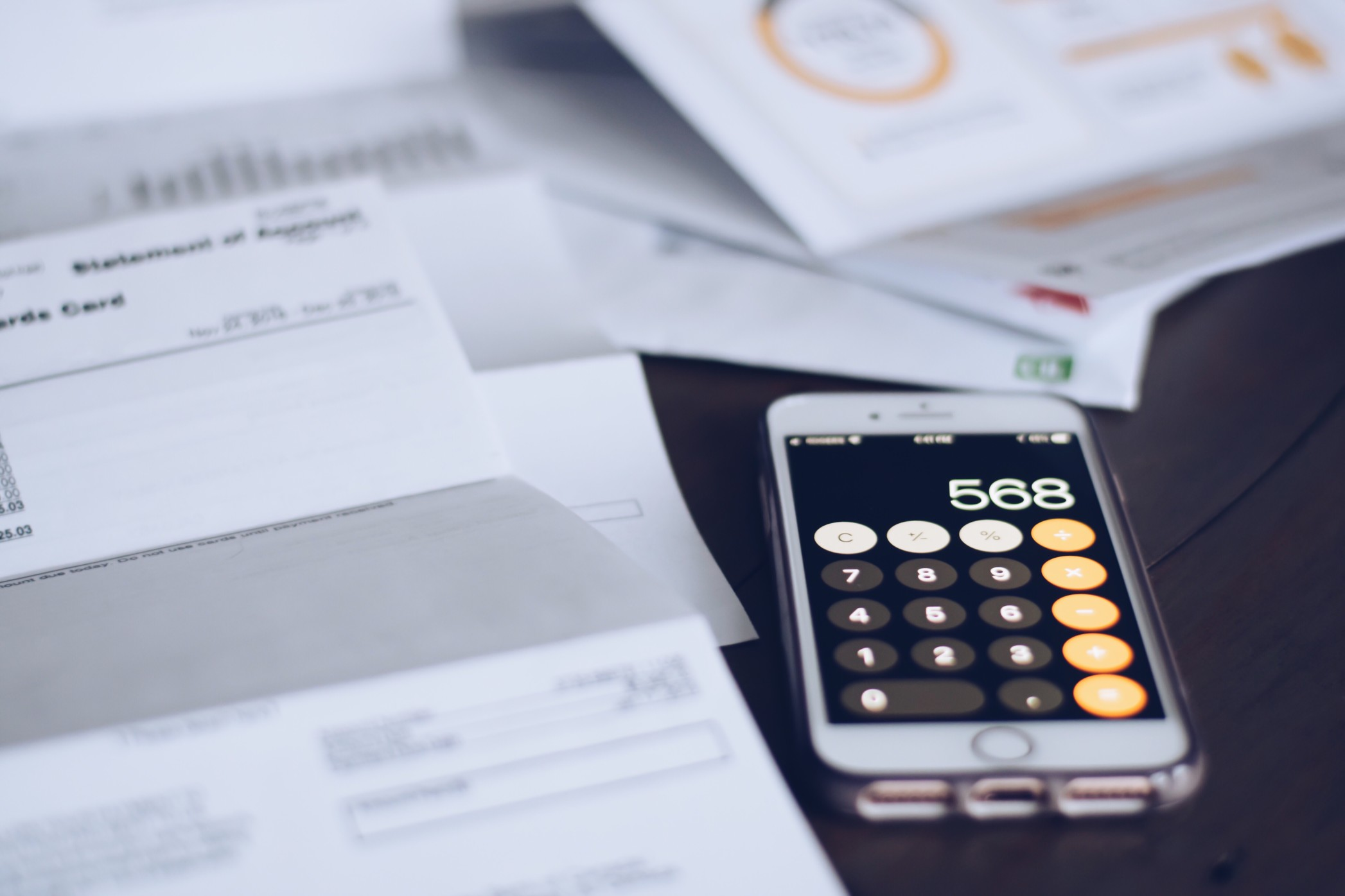 Bills scattered on a table with an iPhone calculator lying next to them, showing the number 568