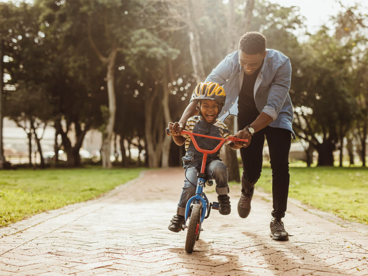 a man is running behind a young boy on a bike, both laughing