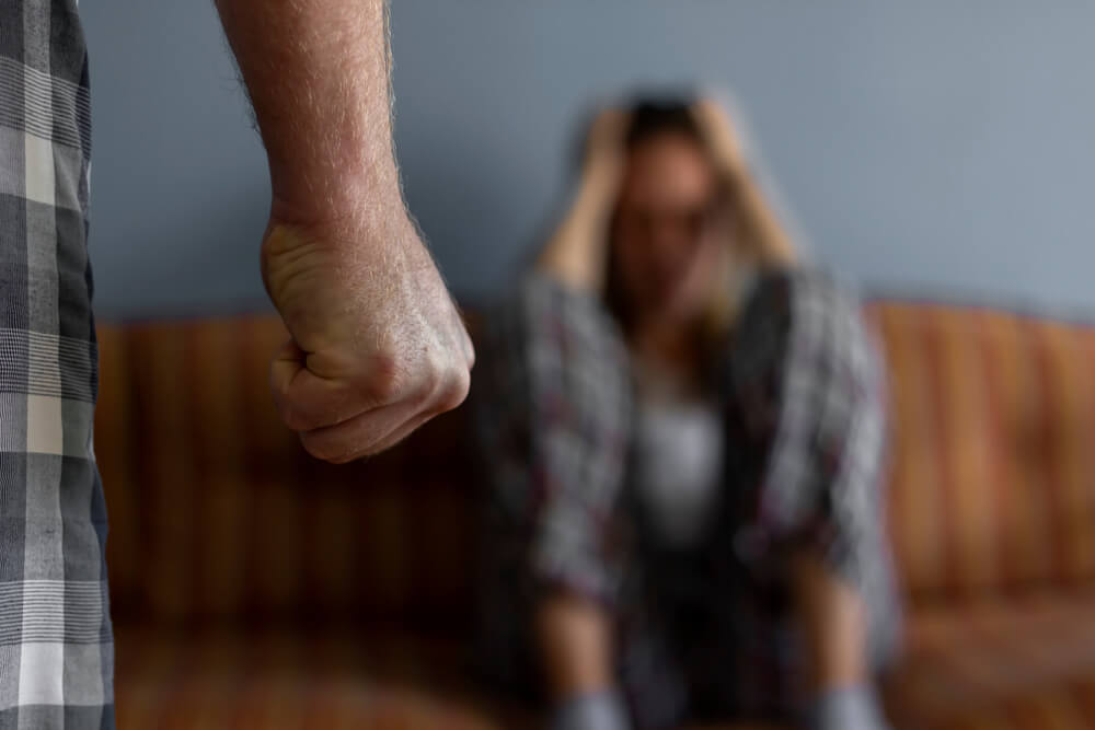 man making a fist while distressed woman is sitting on a couch