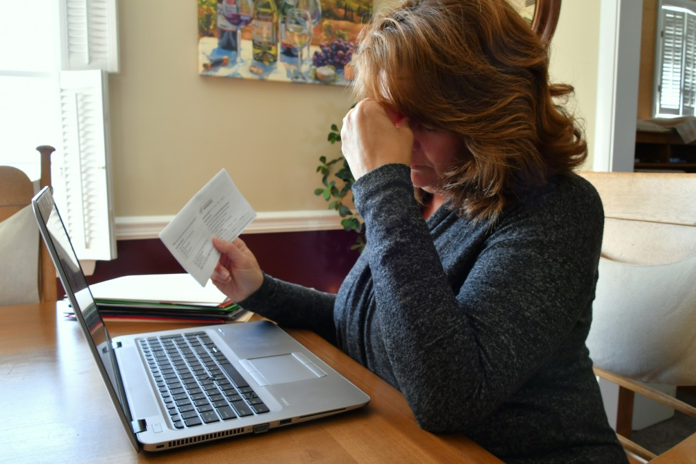 Woman sitting at her computer, holding her hand to her forehead and looking distressed over a bill