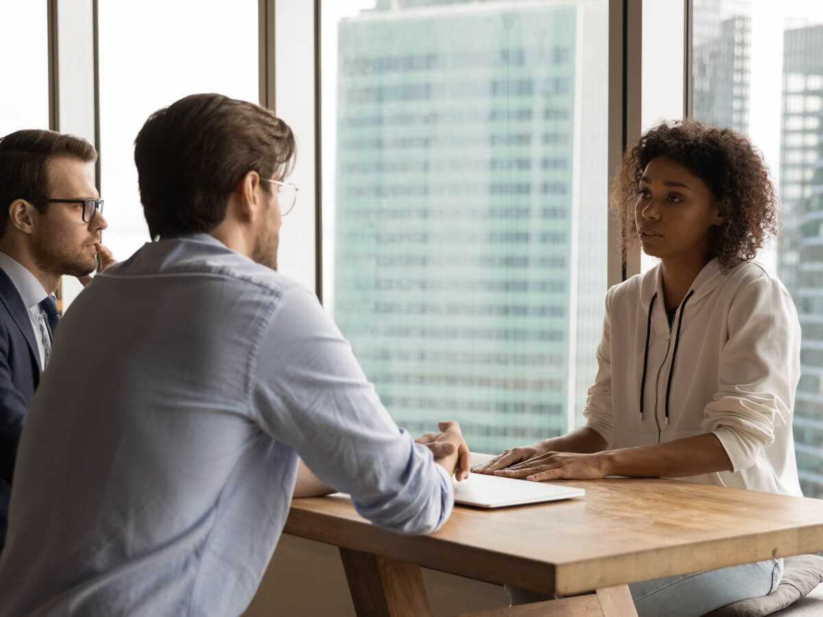 Two men and a woman sitting across from each other with a table between them. The table has a closed laptop on it.