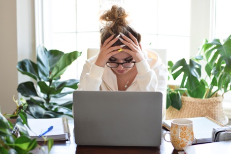 woman staring at computer, feeling stressed with her head in her hands