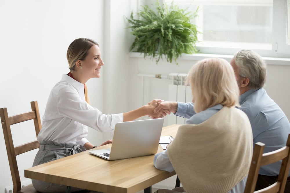 An attorney sitting at a table with an elderly couple, shaking the husband's hand