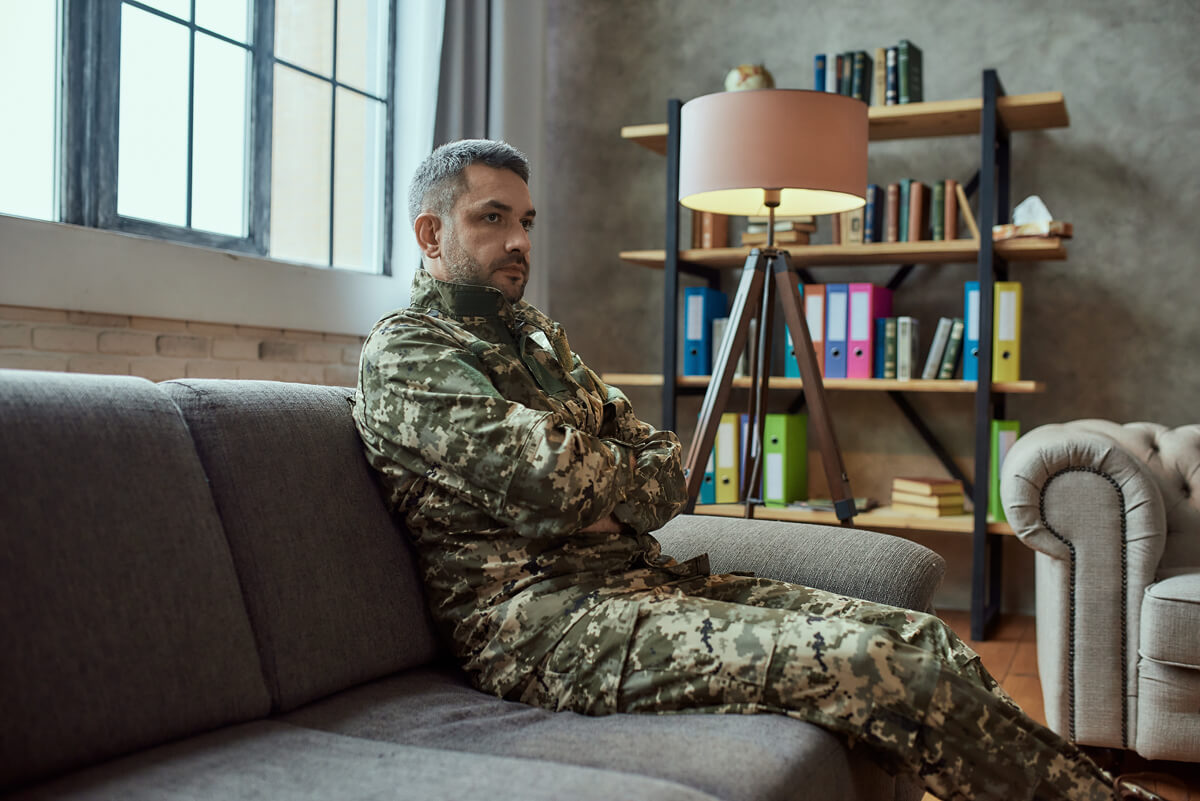A male military servicemember sitting on a couch in uniform