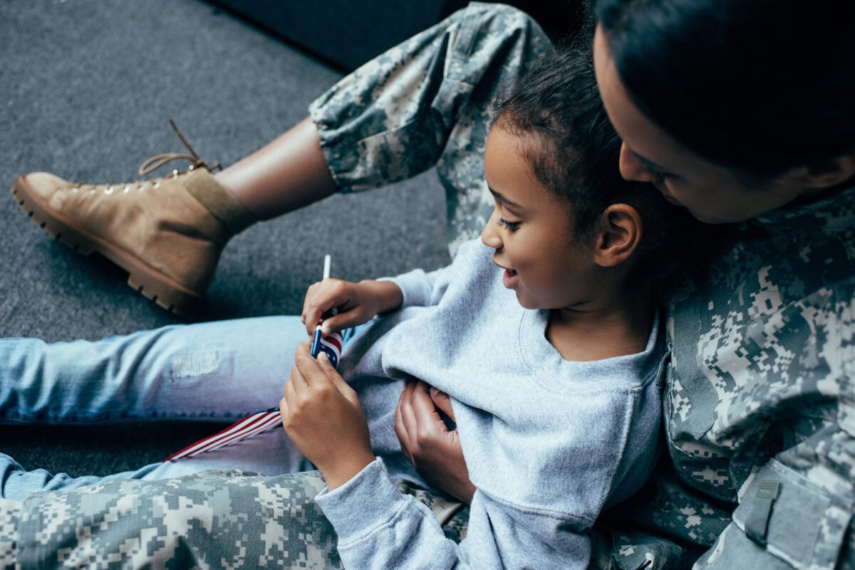 Child and military parent sitting together looking at an American flag